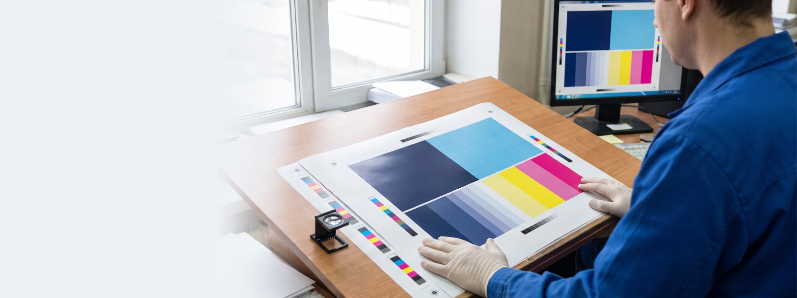 Prepress technician checking a printed proof against a calibrated monitor with a loupe and color bars Prepress technician checking a printed proof against a calibrated monitor with a loupe and color bars
