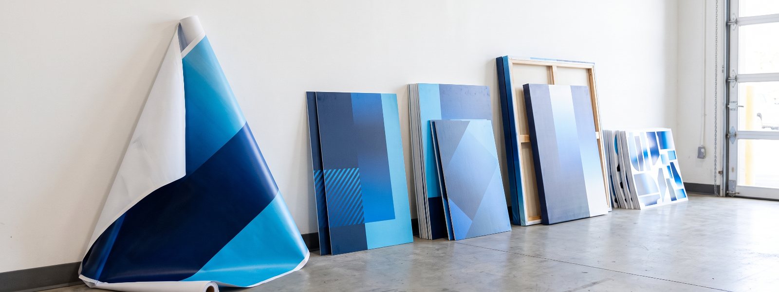 Finished large format printed banners, rigid signs, posters and canvas prints lined up in a San Diego print shop Finished large format printed banners, rigid signs, posters and canvas prints lined up in a San Diego print shop